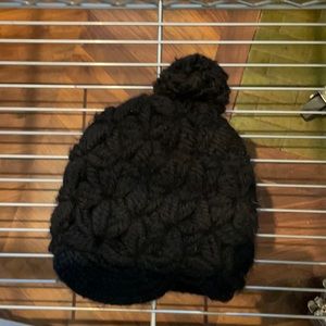 Black knitted cap with small brim, by Eugenia Kim.